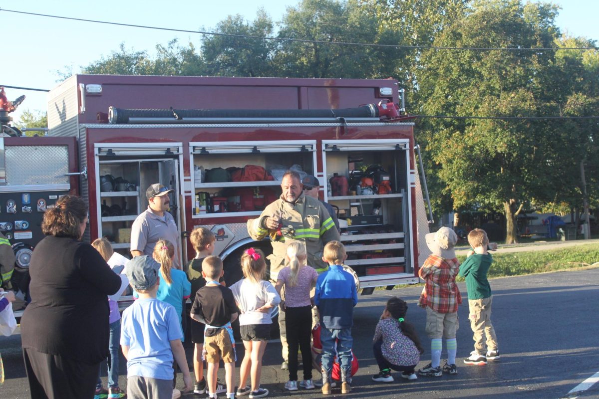 Fire chief discussing the tools in the fire truck with the elementary kids.