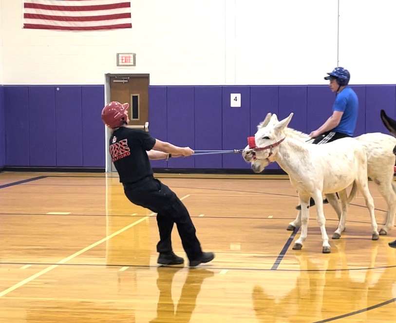 The fire department vs. the police department while playing donkey basketball in the elementary school gymnasium.