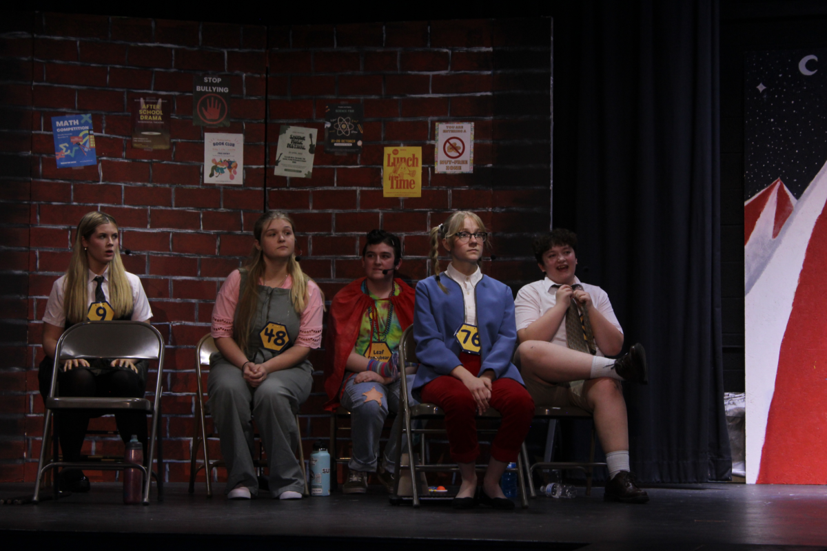 Theater students (left to right) Emma Pearson (understudying for June Chumbley as Marcy Park), Addison Zittle (Olive Ostrovsky), Preston Hicks (understudying for Aubrey Dickens as Leaf Coneybear), Alyssa Faubion (Logainne Schwartzy Schwartzandgrubenierre), and Nico Jenkins (William Barfee) rehearsing for the performance at the Upper Elementary gym stage.