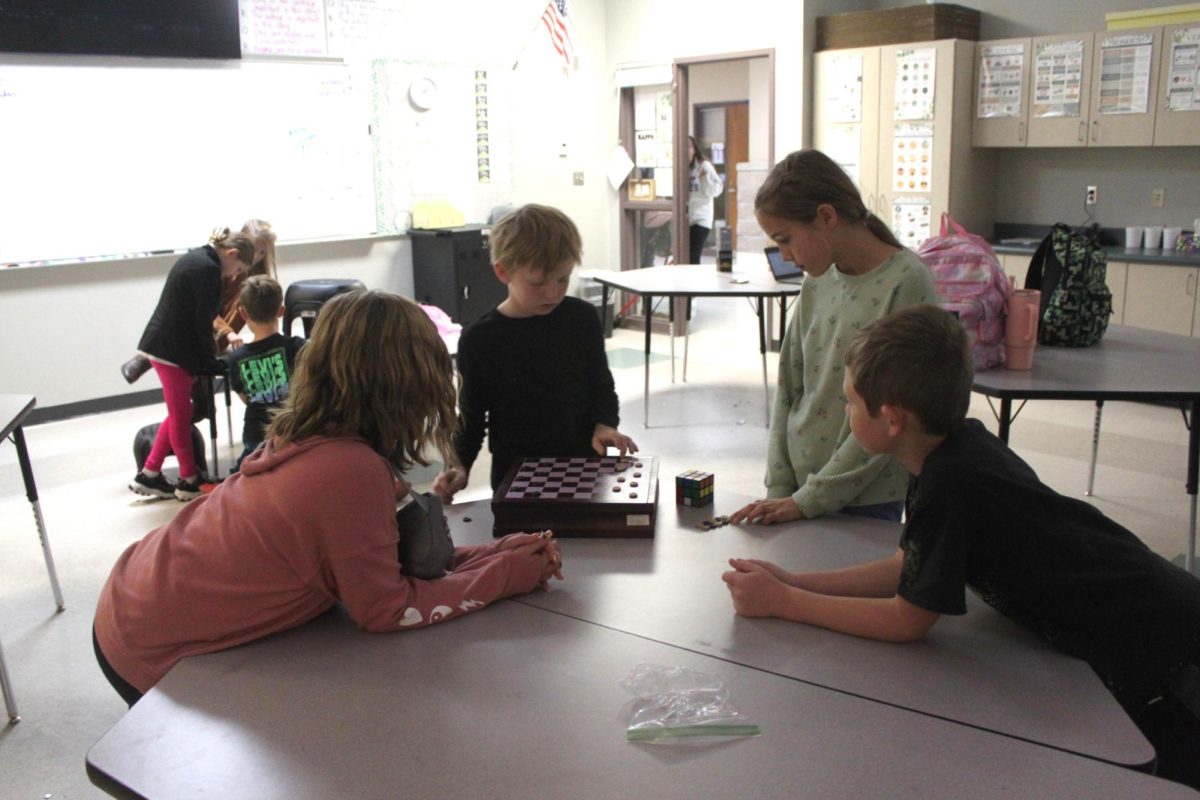 After school Checkers Club taking place in Mrs. Hicks room. Elijah Spangler, Jensen Wilson, Leah Stewart, and Lane Woolery gathering around a checkers board getting ready to play. 