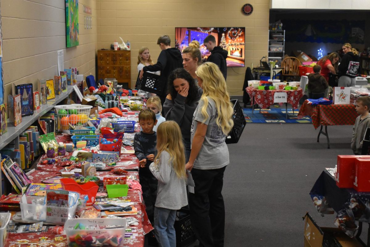 Elementary students shopping in the elementary school library at holiday shop with the assistance of senior students on December 13, 2024 (visible front to back: Timmy Cantwell, Gretta Morris(12), Ashton Bell(12))