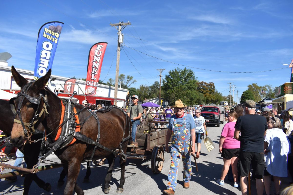 Crowds gather on the streets of Fair Grove for the Fall Festival parade on September 27, 2025. A mule-pulled wagon passes by as people enjoy food and sunny weather.